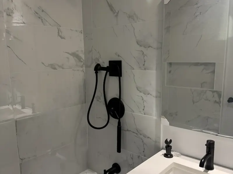 Marble-look large-format tile in a bath surround with black fixtures and slim, evenly spaced grout lines